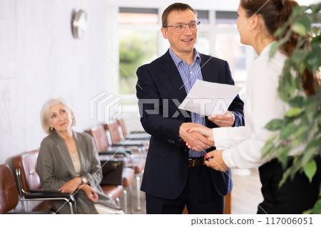 Smiling young girl makes deal, shaking hands with man colleague while standing in office. 117006051