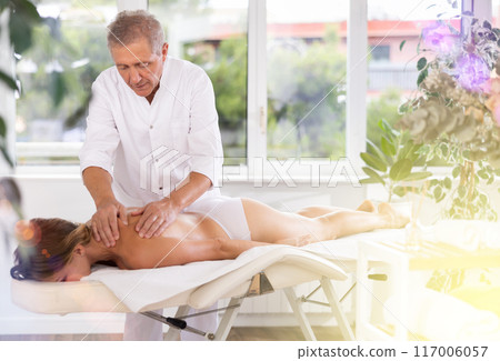 male masseur giving massage to female patient 117006057