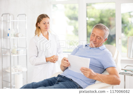 Old male patient signing papers while talking with woman doctor 117006082