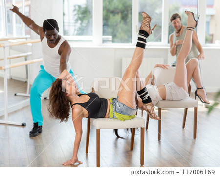 Woman seductively dancing on chair in vibrant studio atmosphere 117006169