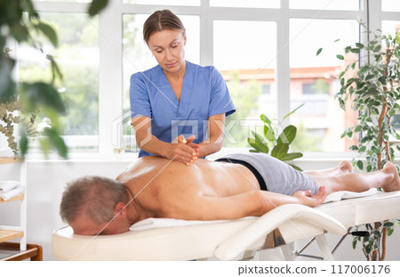 Skilled middle-aged masseuse conducting back massage for man client 117006176