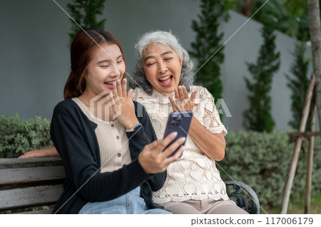 A happy retired Asian grandma is laughing and enjoying talking with her granddaughter in a garden. 117006179