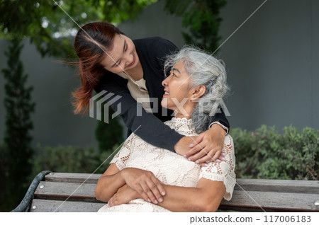 A lovely Asian granddaughter is embracing her grandma with love while resting in a garden together. 117006183