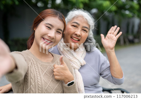 A lovely Asian granddaughter and a happy retired grandma are sitting together on a bench in a park. A lovely Asian granddaughter and a happy retired grandma are sitting together on a bench in a park. 117006213