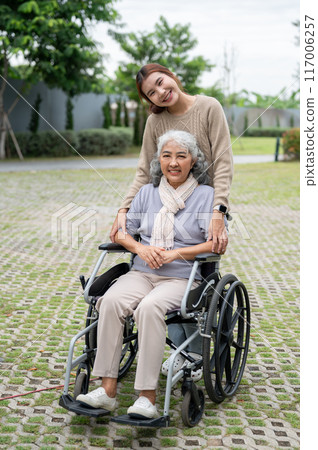 A charming Asian granddaughter and a happy grandmother in a wheelchair are in a park together. A charming Asian granddaughter and a happy grandmother in a wheelchair are in a park together. 117006257
