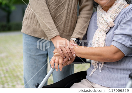 A close-up image of a daughter holding her mom's hand while she is in a wheelchair. A close-up image of a daughter holding her mom's hand while she is in a wheelchair. 117006259