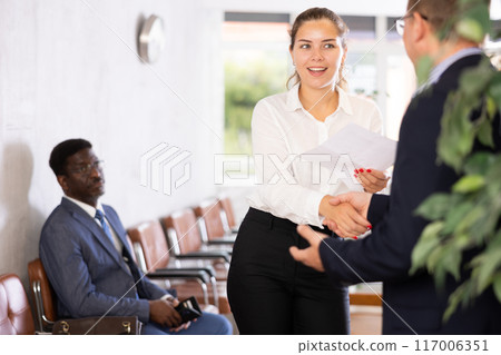 Young woman handshaking with other person in waiting room 117006351