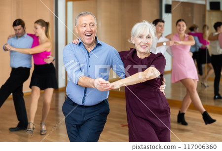 Happy older couple performing a paired ballroom dance in ballroom 117006360