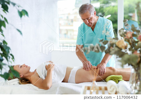 Skilled old masseur conducting hip massage for woman client Skilled old masseur conducting hip massage for woman client 117006432
