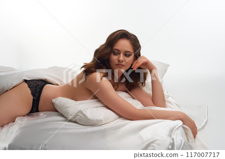 Gentle woman in lace panties lying on white bed 117007717