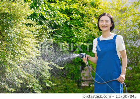 微笑的中年婦女在花園裡的綠樹澆水 微笑的中年婦女在花園裡的綠樹澆水 117007845