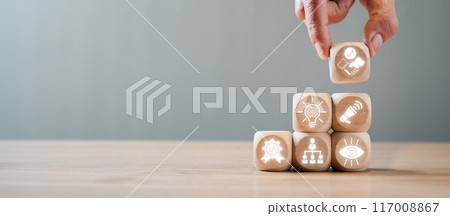 Hand stacking wooden cubes with business icons representing the concept of business excellence on a wooden table. Hand stacking wooden cubes with business icons representing the concept of business excellence on a wooden table. 117008867