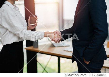 Close-up of two business professionals shaking hands in a modern office environment, symbolizing partnership and agreement. 117008883