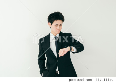 A businessman in his twenties looking at his watch 117011149