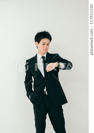 A businessman in his twenties looking at his watch 117011150