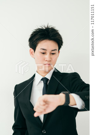 A businessman in his twenties looking at his watch 117011151