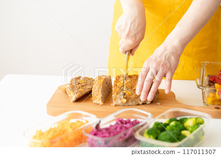 Hands of a woman in a yellow apron cutting meatloaf Hands of a woman in a yellow apron cutting meatloaf 117011307