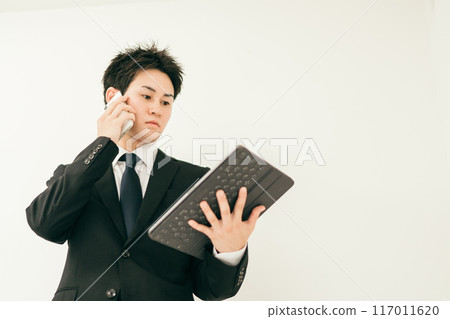 一名20多歲穿著西裝的男子一邊看文件一邊打電話 117011620