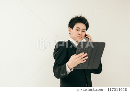 A man in his 20s in a suit talking on the phone while looking at documents A man in his 20s in a suit talking on the phone while looking at documents 117011628