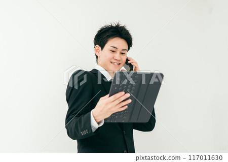 A man in his 20s in a suit talking on the phone while looking at documents A man in his 20s in a suit talking on the phone while looking at documents 117011630