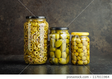 Pickled green olives in brine in jar on black table. 117011964