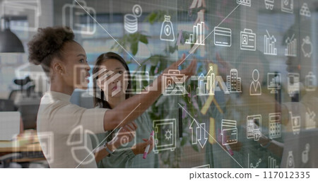 Image of business media logos over diverse female colleagues brainstorming at casual office 117012335