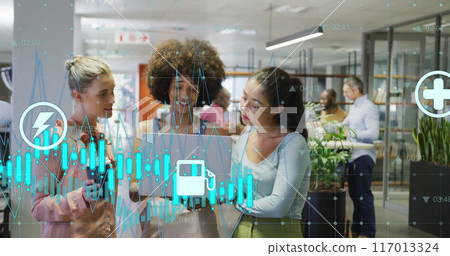 Image of graph and energy icons over diverse female colleagues using laptop at casual office Image of graph and energy icons over diverse female colleagues using laptop at casual office 117013324
