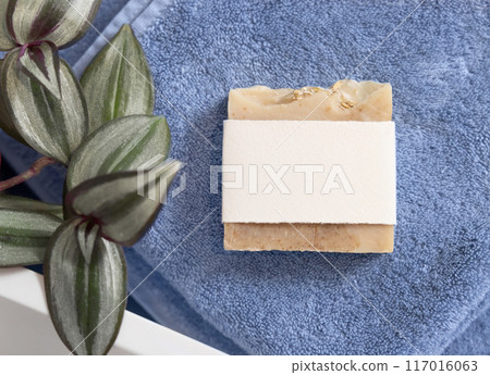 Soap bar with blank label on blue folded towel near green plant top view, packaging mockup Soap bar with blank label on blue folded towel near green plant top view, packaging mockup 117016063