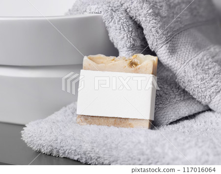 Soap bar with blank label on light grey towels near vessel sink in bathroom closeup, mockup 117016064
