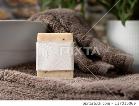 Soap bar with blank label on brown folded towels near plant and basin in bathroom, mockup Soap bar with blank label on brown folded towels near plant and basin in bathroom, mockup 117016069