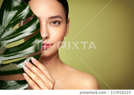 Close up woman face with green exotic leaf Close up woman face with green exotic leaf 117016225