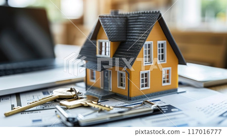 A model house placed on a desk with a key lying next to it, surrounded by real estate documents and a laptop, symbolizing a property deal. 117016777
