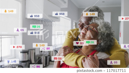 Social media interaction icons image over elderly couple embracing in kitchen 117017711