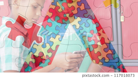 Jigsaw puzzle and ribbon icon against two diverse boys using smartphone at school 117018073