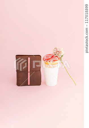 Donut on top of disposable coffee cup, notebook and dried flower on pink background. 117018899