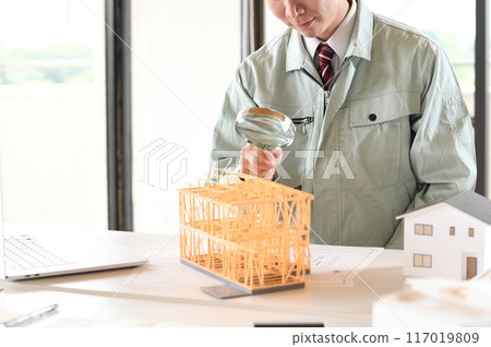 一個穿著工作服的男人用放大鏡看著建築模型 117019809
