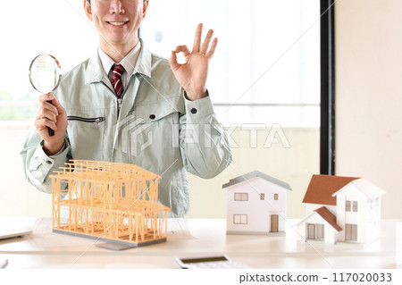A man in work clothes holding a magnifying glass in front of an architectural model 117020033
