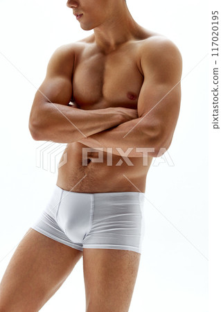 Cropped photo of young man posing in boxers crossed hands on breast against white studio background, shows his well-defined abs and chest. Cropped photo of young man posing in boxers crossed hands on breast against white studio background, shows his well-defined abs and chest. 117020195