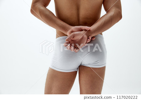 Rear view photo of fit man in boxers posing holds hands behind his back, highlighting his toned physique against white studio background 117020222