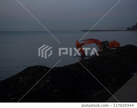 Excavator work at night. Overtime work. The work of construction equipment on the seashore. Batumi. Fortified shores. at sunset. Excavator work at night. Overtime work. The work of construction equipment on the seashore. Batumi. Fortified shores. at sunset. 117020344