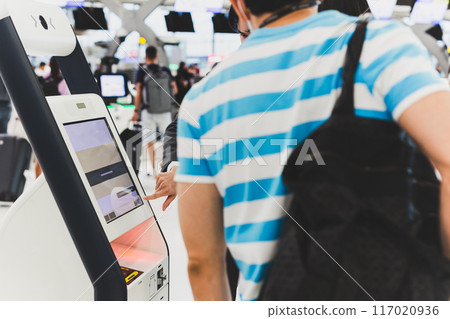 Male passenger with backpack  doing self check in for flight at automatic device in modern airport. 117020936