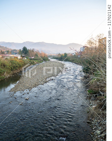 A shallow fast river. Stream with shallows. Fast river in the city. Concrete rapids on the river. River in Georgia. A shallow fast river. Stream with shallows. Fast river in the city. Concrete rapids on the river. River in Georgia. 117021142