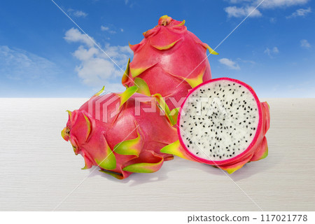 Dragon fruit, red-green peel fruit isolated on a white wooden table with a bright sky in the background Dragon fruit, red-green peel fruit isolated on a white wooden table with a bright sky in the background 117021778
