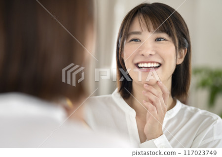 A woman in her early 30s smiling while looking in the mirror A woman in her early 30s smiling while looking in the mirror 117023749