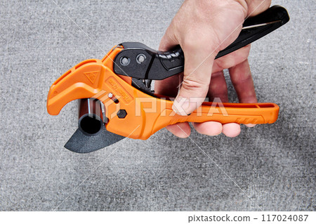 Scissors cutter for cutting pipes with ratchet mechanism, in man hand on gray background. Scissors cutter for cutting pipes with ratchet mechanism, in man hand on gray background. 117024087