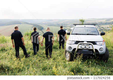 A team of courageous rescuers in black uniforms standing in nature in a field 117024256
