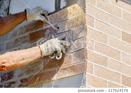 Installing brick veneer outside, construction worker decorates facade of house with exterior panel of fake thin brick. 117024579