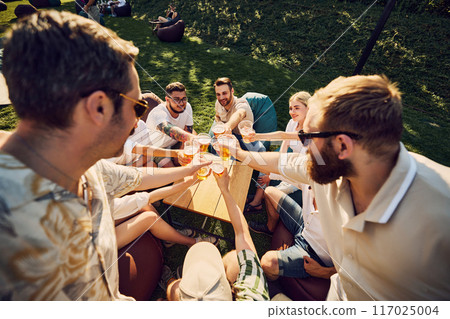 Birthday celebration. Happy young people, men and women, friends clinking beer glasses, spending lovely time outdoors. Picnic 117025004