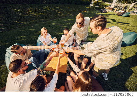 Birthday celebration. Happy young people, men and women, friends clinking beer glasses, spending lovely time outdoors. Picnic 117025005