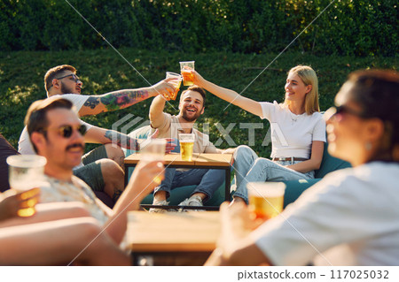 Positive young men and women,friends gathering outdoors in public place, enjoying company, conversation and beer 117025032